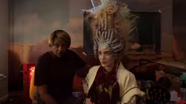 Two people seated together one wearing an elaborate sculptural headdress