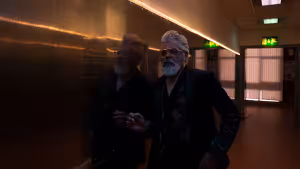 Two men with white hair and beards walking through a dimly lit corridor