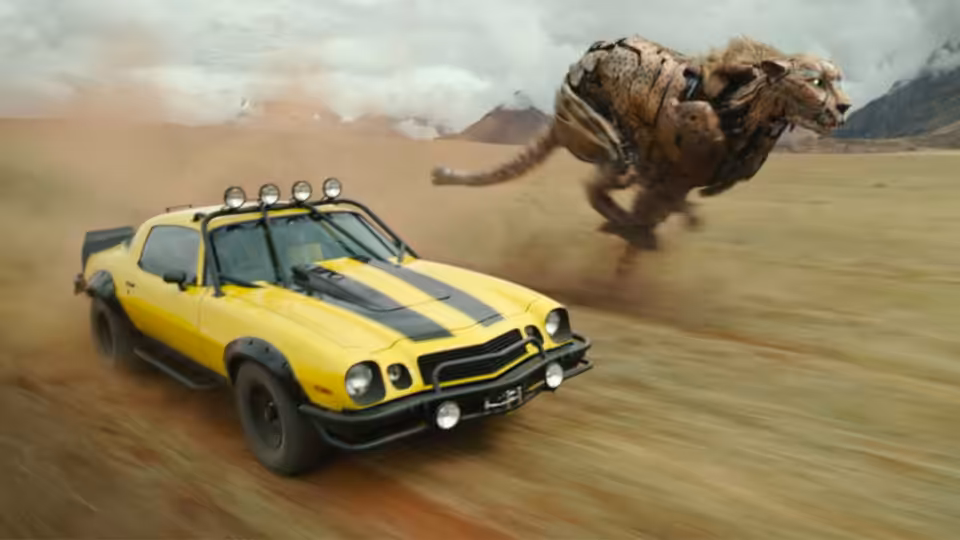 Yellow muscle car speeding across desert sand with robotic beast leaping behind