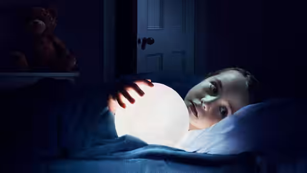 Sawyer Harper (Vivien Lyra Blair) holding a glowing orb while lying in bed