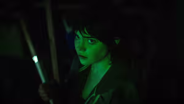 Sadie Harper (Sophie Thatcher) gripping a glowing rod in a dark cluttered space