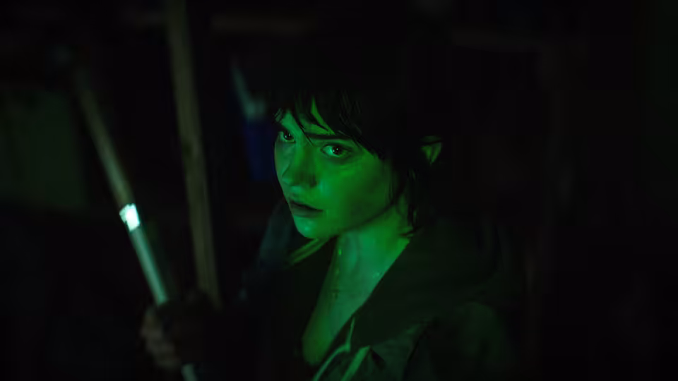 Sadie Harper (Sophie Thatcher) gripping a glowing rod in a dark cluttered space