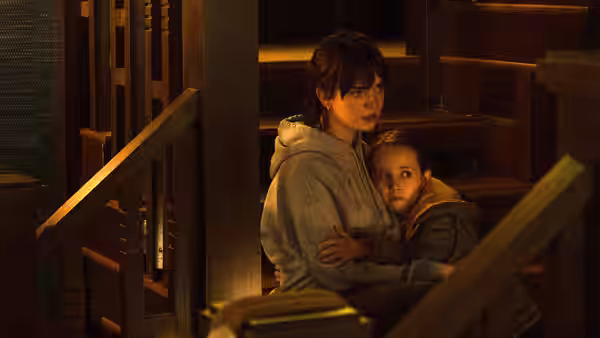 Sadie Harper (Sophie Thatcher) holding Sawyer Harper (Vivien Lyra Blair) on wooden stairs