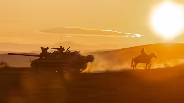 a tank fires while a rider on horseback gallops alongside at sunset