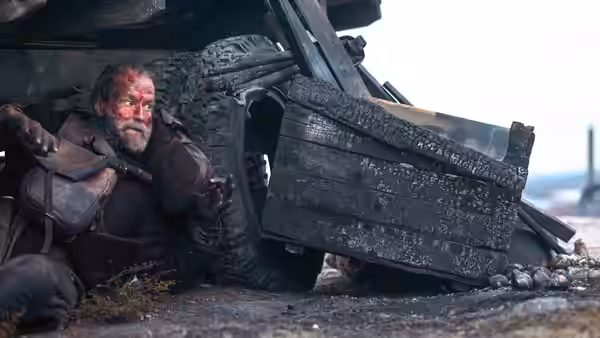 Aatami (Jorma Tommila) crouches wounded beneath the wreckage of a vehicle