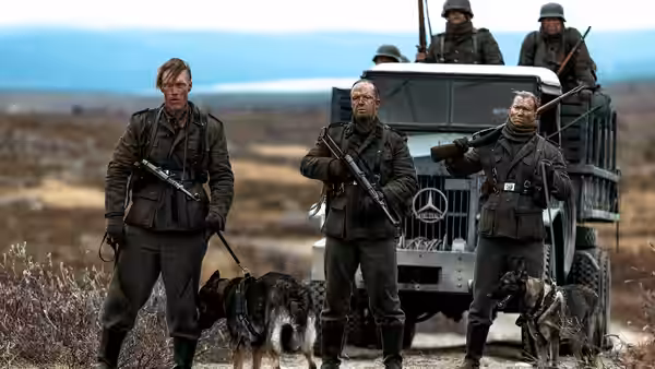 three soldiers stand with dogs in front of an army truck