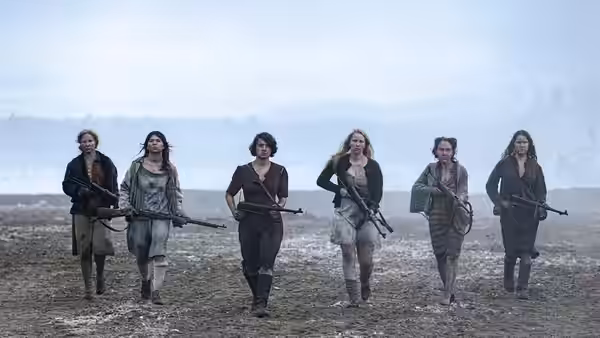 five armed women walk in formation across a barren landscape