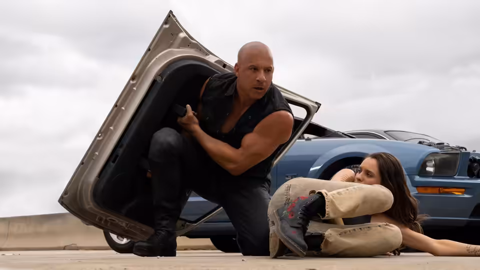 Dominic Toretto (Vin Diesel) crouches by an open car door over a woman on the ground