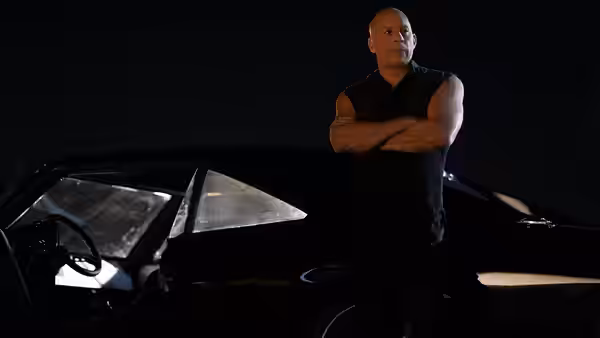 Dominic Toretto (Vin Diesel) stands with arms crossed beside a black car at night