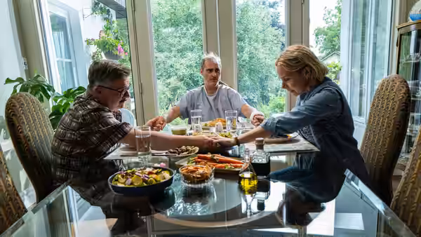 Beau Wassermann (Joaquin Phoenix) holding hands with two others at a dining table