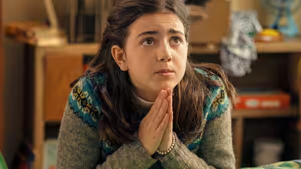 A girl clasps her hands and looks upward with concern