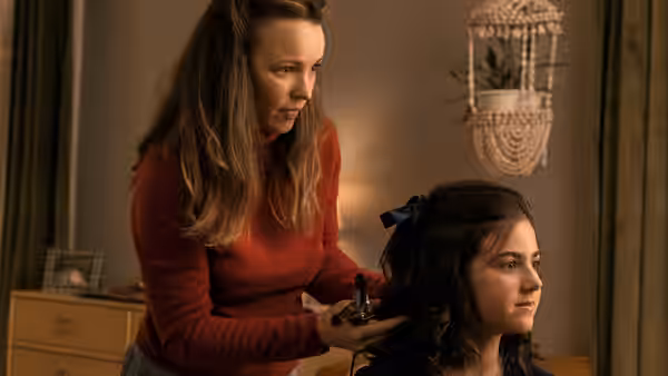 A woman in a red sweater styles a girl's hair
