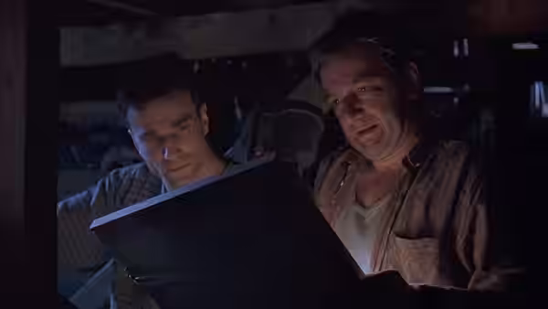 Danny Flynn and an older man examine a large open book in a dim room