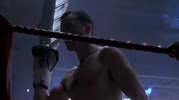 Danny Flynn, wearing boxing gloves, leans against the ropes inside a boxing ring