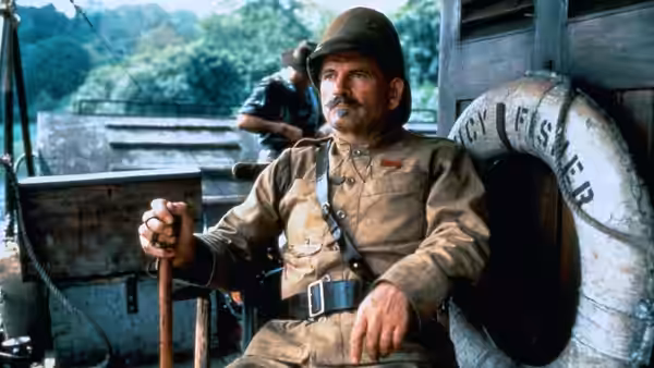 A mustached uniformed man sits aboard a rail vehicle, with another man behind him