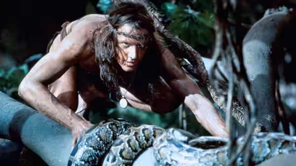 Tarzan (Christopher Lambert) crouches over a large snake in the jungle