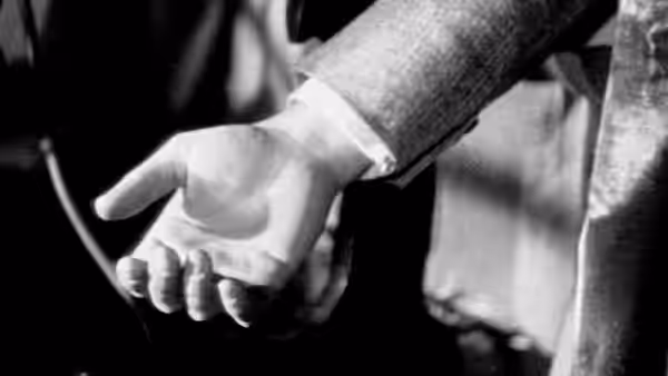 A man’s hand grips a knife beside another person’s clothing