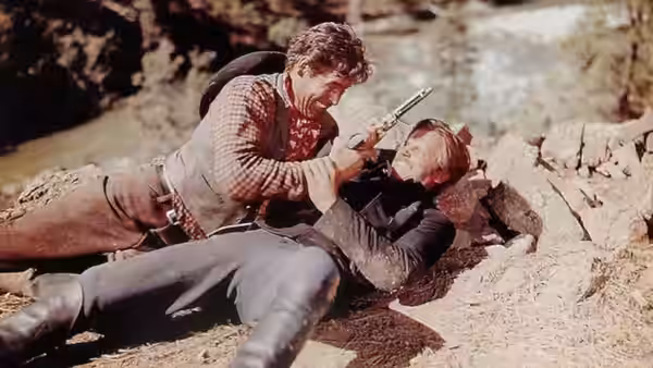 A man in a plaid shirt wrestles another man for a revolver on rocky ground
