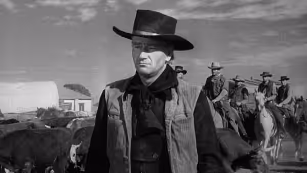 Thomas Dunson (John Wayne) stands among cattle and mounted cowboys
