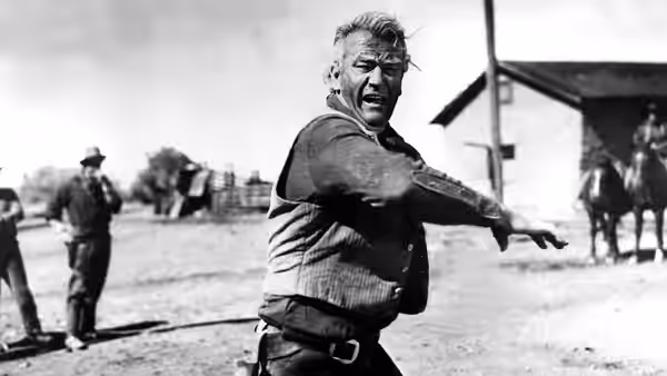 Thomas Dunson (John Wayne) gestures across a ranch yard