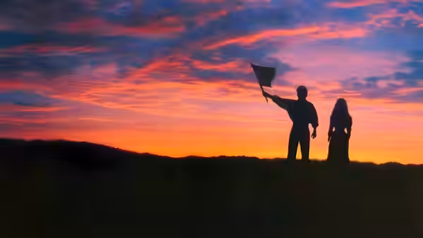 Joseph Donnelly raises a hat beside Shannon Christie on a hill at sunset