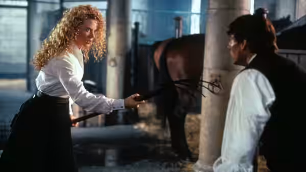 Shannon Christie holds a riding crop toward Joseph Donnelly in a stable