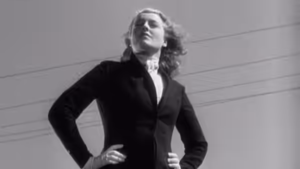 Princess Jeanette stands with hands on hips against a plain wall