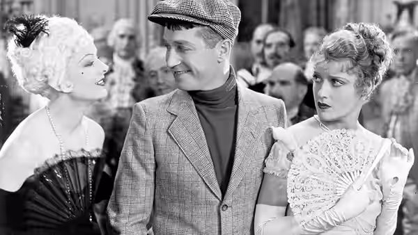 Maurice Courtelin stands between two women at a gathering as they look toward him