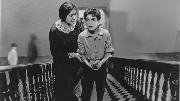 A woman steadies a boy on a staircase, leaning close as he looks ahead