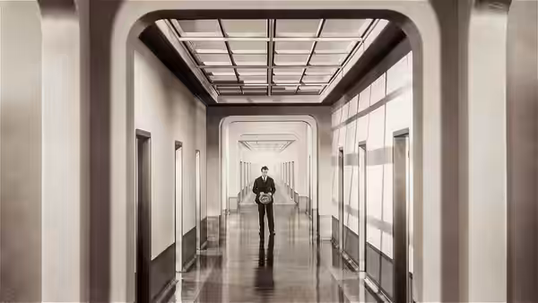 A suited man stands alone in a long office corridor
