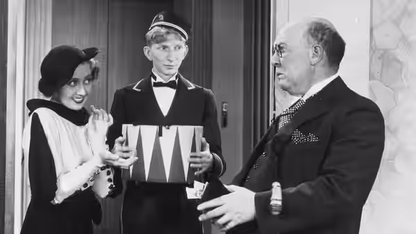 A uniformed attendant holds a box between a woman and an older man