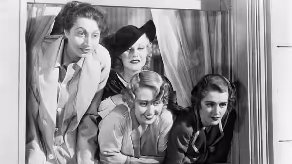Four women lean out through a curtained window to look inside