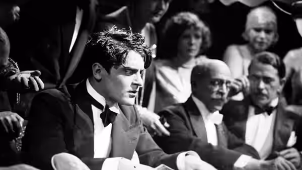 Alwa Schön (Francis Lederer) sits among formally dressed spectators at a theater