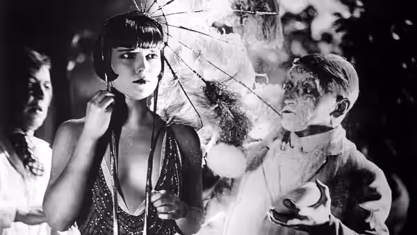 Lulu (Louise Brooks) poses beneath an open parasol as a man tends to her