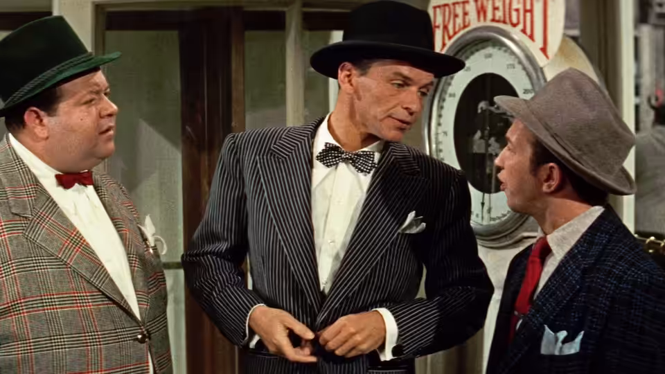Sky Masterson (Marlon Brando) stands between two men in hats inside a club
