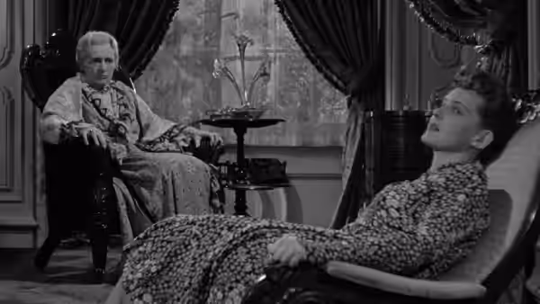 Dr. Jaquith (Claude Rains) watches Charlotte recline in his office