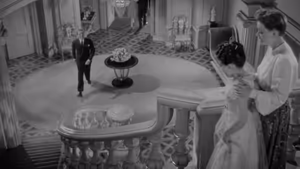 A woman stands with another woman on a landing as a man approaches