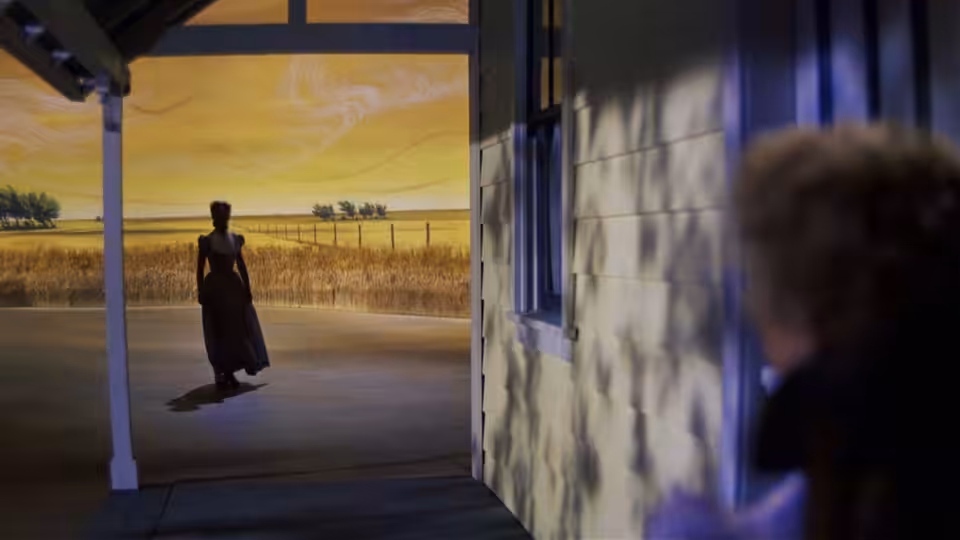 A lone man stands in a doorway, looking across a fenced prairie