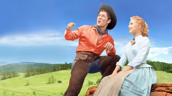 Curly McLain (Gordon MacRae) gestures from a wagon as Laurey Williams (Shirley Jones) watches