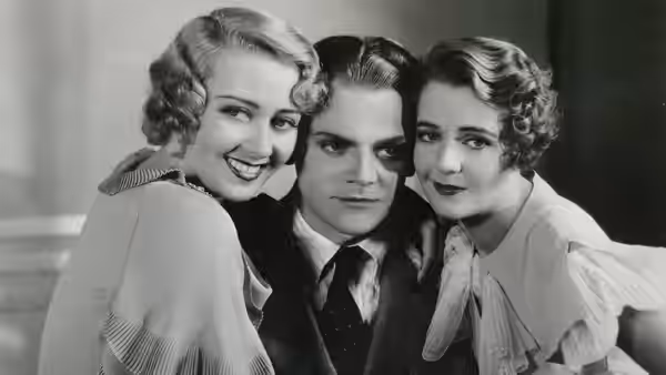 Two women lean close beside a suited man facing the camera