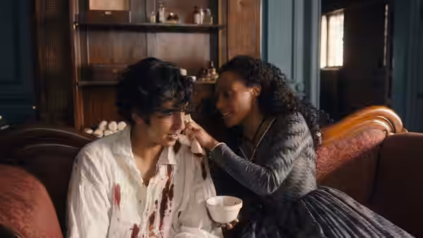 A woman feeds David Copperfield as he sits with a bowl in a sitting room