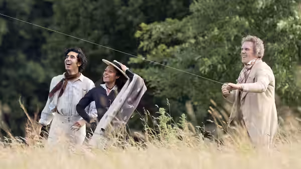 David Copperfield, a woman carrying fabric, and an older man walk through a grassy field