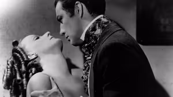 Armand Duval (Robert Taylor) leans over Marguerite Gautier (Greta Garbo) as she reclines