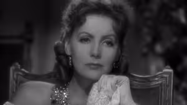 Marguerite Gautier (Greta Garbo) sits in a chair holding a lace handkerchief