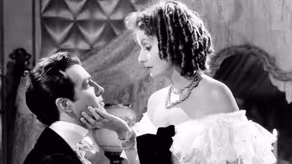 Marguerite Gautier (Greta Garbo) cups Armand Duval’s face in an elegant room