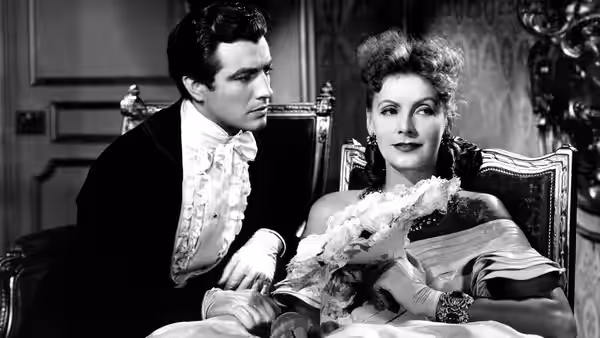 Armand Duval (Robert Taylor) sits beside Marguerite Gautier (Greta Garbo), who holds a bouquet