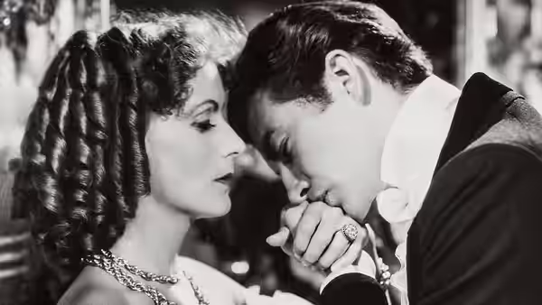 Armand Duval (Robert Taylor) kisses Marguerite Gautier’s hand as she watches him