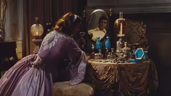 A woman in a lavender gown sits at a dressing table, studying her reflection