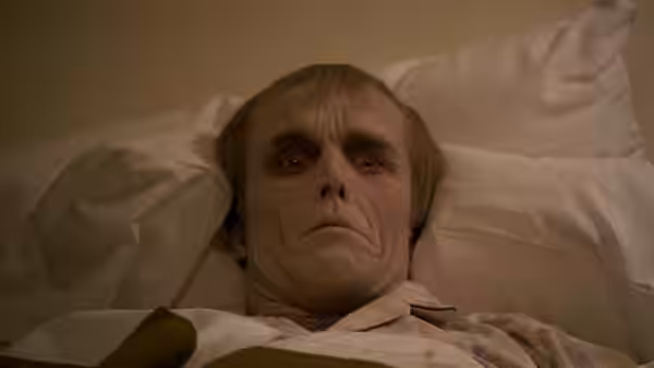 A pale man with wide eyes lies in bed staring ahead