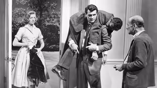 A woman watches as a man adjusts his suit beside an older man